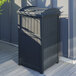 A dark gray rectangular Suncast trash container with a white lid on a deck.