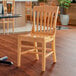 A Lancaster Table & Seating natural finish wood school house chair on a wood floor in a restaurant dining area.