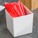 A white square melamine jar on a counter with red straws in it.