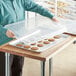 A woman putting a plastic lid on a Choice full size aluminum sheet pan of cookies.