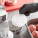 A hand holding a round white Garde perforated patty paper with black glove.