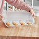 A woman's arm reaching out to a plastic container with a Baker's Mark bun / sheet pan cover on it.