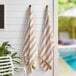 Two Monarch Brands beige striped pool towels hanging on a wall.