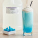 A white container of blue liquid labeled "LorAnn Oils Blue Raspberry Super Strength Flavor" on a counter next to a blue drink with a straw.