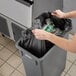 A woman's hand putting a black Lavex Hercules trash bag into a trash can.