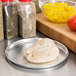 An American Metalcraft aluminum pizza pan with a ball of dough on it next to a bowl of peppers and other ingredients.