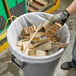 A gloved hand placing a Lavex Pro clear trash bag full of wood in a trash can.