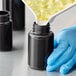 A gloved hand in blue pouring yellow pills into a dark amber packer bottle.
