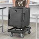 A man holding a black Choice front-loading food pan carrier on a counter in a professional kitchen.