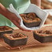 A person holding a Novacart brown paper baking mold filled with food on a tray.