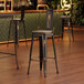 A Lancaster Table & Seating distressed copper metal barstool with a gray wood seat at a bar.