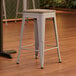 A Lancaster Table & Seating nickel gray metal backless counter height stool with a gray wood seat.