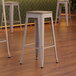 Three Lancaster Table & Seating white metal backless bar stools with gray wood seats.