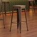 Three Lancaster Table & Seating copper barstools with gray wood seats on a wood floor.