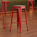 A close-up of a red Lancaster Table & Seating backless barstool with a gray wood seat.