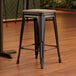 A Lancaster Table & Seating Onyx Black backless counter height stool with a gray wood seat.