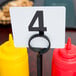 A rectangular wrought iron condiment caddy with a card holder on a table with a number four.