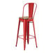 A red metal Lancaster Table & Seating barstool with a wood seat.