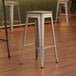 Three Lancaster Table & Seating silver metal barstools with gray wood seats.