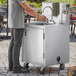 A man standing next to a Regency stainless steel portable hand sink on a counter in an outdoor catering setup.