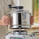 A man using a silver AvaMix stainless steel bowl with an "S" blade in a food processor on a counter in a professional kitchen.