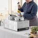 A woman in a chef's uniform using a Galaxy electric countertop food warmer to prepare food.