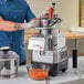 A man in a blue uniform and gloves using an AvaMix stainless steel bowl on a food processor to shred carrots.