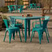 A Lancaster Table & Seating teal table and chairs outside on a stone patio.