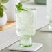 An Acopa Pangea green goblet with ice and mint on a table.