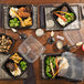 A table with Pactiv Earthchoice black plastic containers of food.
