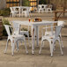 A Lancaster Table & Seating white metal table and chairs on an outdoor patio.