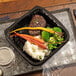 A black Pactiv Earthchoice dual-color plastic take-out container with food inside.