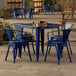 A blue metal Lancaster Table & Seating outdoor table with four blue chairs on a stone patio.