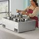 A woman in an apron using a ServIt countertop food warmer to cook food.