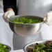 A person in gloves holding a close-up of a stainless steel mixing bowl filled with salad.