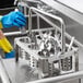 A person in blue gloves cleaning stainless steel flatware in a metal sink.