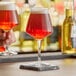 A Rastal Teku beer glass filled with red liquid on a table in a bar.