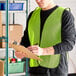 A lime high visibility mesh safety vest being worn by a person in a warehouse setting.