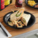 A Fineline black polypropylene plate with a sandwich and pasta on it.