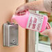 A person pouring pink liquid from a bottle into a soap dispenser.