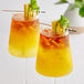 Two glasses of Les Vergers Boiron yellow and orange tropical fruit drinks with ice and fruit garnish.