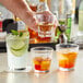 A man pouring drinks into Acopa Memphis rocks glasses on a table in a cocktail bar.