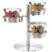 A Cal-Mil stainless steel three tier jar display on a table with metal jars and a bowl.