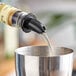 A person using a black liquor pourer to pour liquid into a container.