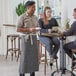 A man in an Acopa Kennett gray denim bistro apron serving a woman at a table.