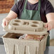 A woman wearing a green apron holding a Fiber Cooler Lid on a container of food.