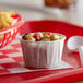 A white paper souffle cup filled with food on a red tray.