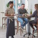 A man and woman sitting at a table with a man and woman standing behind them. A man wearing a blue denim Acopa Kennett bistro apron.