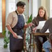 A man and woman dining in a restaurant with a man wearing a blue denim Acopa Kennett apron.