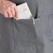 A person's hand putting a piece of paper in the pocket of an Acopa Kennett Gray Denim Bib Apron.